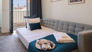 Ett hotellrum med en säng, en soffa, en balkong med utsikt och ett brickbord med en kopp och en bok.