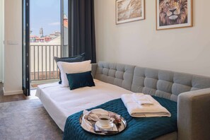 Ein Hotelzimmer mit Bett, einer Couch, einem Balkon mit Blick und einem Tablett mit Tasse und Buch.