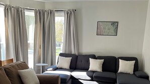 Ein modernes Wohnzimmer mit einem braunen Sofa, einem schwarzen Ecksofa, einem weißen Couchtisch und Blick ins Freie durch große Fenster.