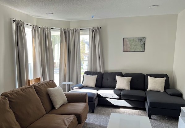 A living room with a brown sofa, a black sectional sofa, and a white coffee table.