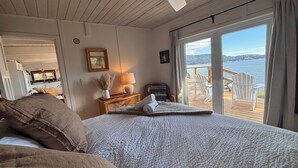 Un dormitorio con cama, mesita de noche, lámpara, ventana con vista al agua y ventilador de techo.