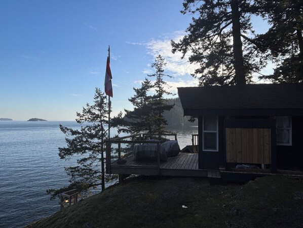 A cabin with a deck overlooking a lake, surrounded by trees.