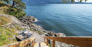 A wooden deck with chairs overlooking a rocky shoreline and calm water.