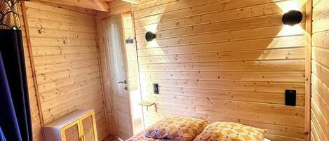 Ein Zimmer in einer Holzhütte mit einem Bett, einem kleinen Schrank und einem Heizgerät.