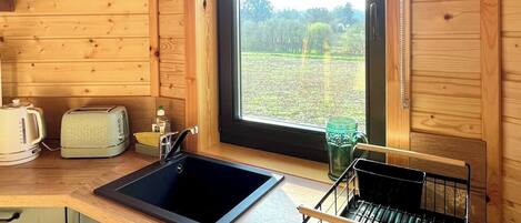 A wooden cabin kitchen with a window, a sink, a toaster, and a dish rack.