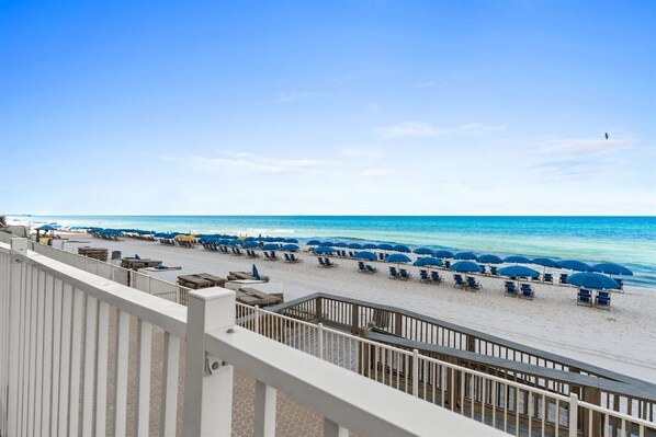 A beach with rows of sun loungers and umbrellas, a wooden deck, and a clear view of the ocean. - Luxury Beachfront 2BR Sleeps 8 Pool Amazing Views (Panama City Beach)