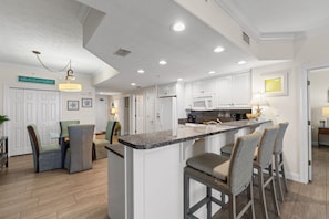 A modern kitchen with white cabinetry, granite countertops, and a central island with bar stools. - Luxury Beachfront 2BR Sleeps 8 Pool Amazing Views (Panama City Beach)