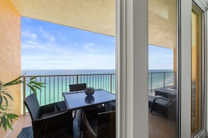 A balcony with a table and chairs, a view of the ocean, and a plant. - Luxury Beachfront 2BR Sleeps 8 Pool Amazing Views (Panama City Beach)