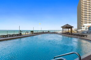 A swimming pool with a gazebo, a tall building, and a flagpole. - Luxury Beachfront 2BR Sleeps 8 Pool Amazing Views (Panama City Beach)