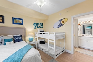 Een slaapkamer met een stapelbed, een bed met kussens, een nachtkastje met een lamp en een muur met een foto en een bord.