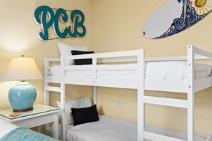 A bunk bed room with a wall-mounted surfboard decoration and a lamp on a bedside table. - Luxury Beachfront 2BR Sleeps 8 Pool Amazing Views (Panama City Beach)