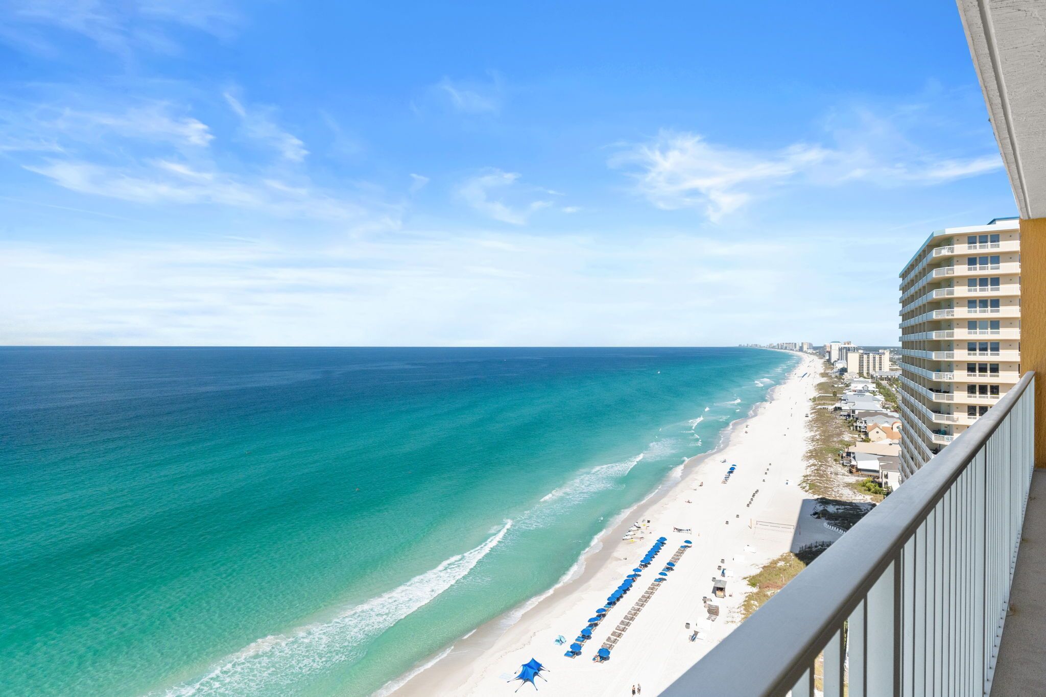 A beach view from a balcony overlooking a sandy beach with a clear blue sky.