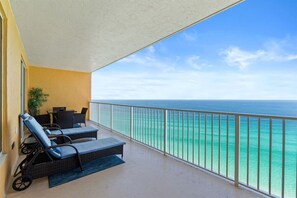 A balcony with two lounge chairs and a table, overlooking a clear blue sea. - Luxury Beachfront 2BR Sleeps 8 Pool Amazing Views (Panama City Beach)