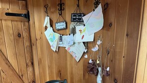 A wooden dining table with a woven placemat, a red vase, and a check-in sign on the wall. - Tiny Timber frame 1-bedroom cabin in Candor with AC/Heat, Outdoor fire and tub. (Candor)