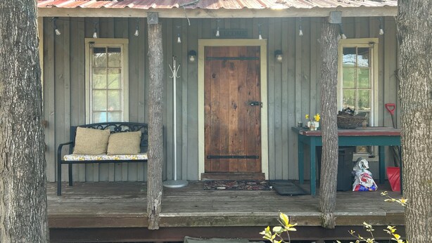 A rustic wooden porch with a bench, a door, and a small table with items on it. - Tiny Timber frame 1-bedroom cabin in Candor with AC/Heat, Outdoor fire and tub. (Candor)