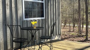 A wooden deck with a table and chairs, a window, and a view of trees. - Tiny Timber frame 1-bedroom cabin in Candor with AC/Heat, Outdoor fire and tub. (Candor)