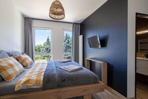 Ein Schlafzimmer mit Bett, Fernseher und einem Fenster mit Blick auf Bäume.