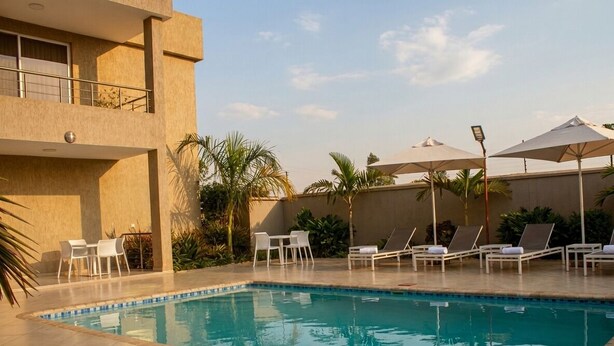 Una piscina con sillas de descanso y sombrillas, rodeada por un edificio con balcón.