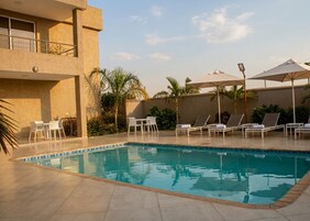 Una piscina con sillas de descanso y sombrillas, rodeada por un edificio con balcón.