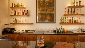 Zona de bar con estantes llenos de botellas de licor, una máquina de café y un cuadro con un paisaje boscoso.