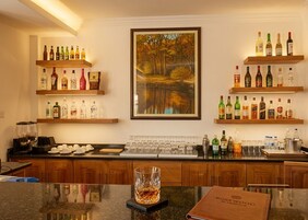 Zona de bar con estantes llenos de botellas de licor, una máquina de café y un cuadro con un paisaje boscoso.