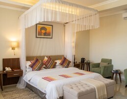 Un dormitorio con cama con dosel, una lámpara de noche, un sillón verde y una mesita con un libro y una tetera.