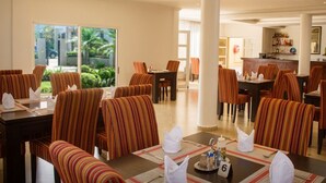 Comedor de hotel con sillas y mesas a rayas, una zona de bar y vistas a zonas verdes.