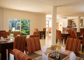Comedor de hotel con sillas y mesas a rayas, una zona de bar y vistas a zonas verdes.