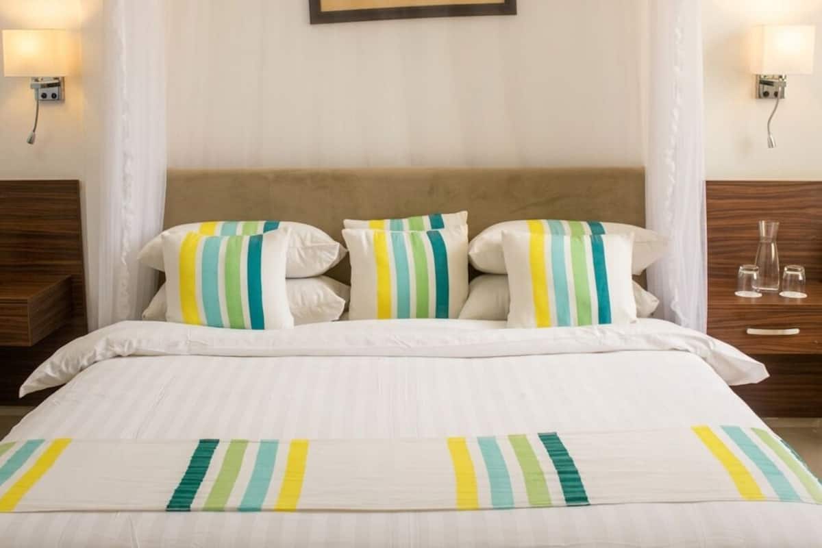 A hotel room with a bed, striped pillows, a painting on the wall, and bedside lamps.