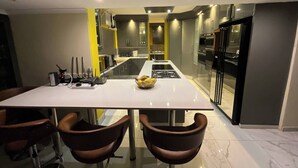A modern kitchen with a central island, stainless steel appliances, and a dining area with a white table and brown chairs. - Room-a Peaceful and Scenic Area Designed (Cape Town)