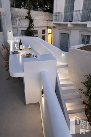 A modern outdoor dining area with a white table and chairs, a bottle of wine, and a glass of white wine.