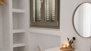 A room with a white vanity, a wooden chair, a mirror, and a shelf with baskets. - Naxos Damarionas Retreat | Newly Renovated Cycladic House with Views (Damarionas)