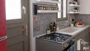 A kitchen with a gas stove, white cabinets, and a tiled backsplash. - Naxos Damarionas Retreat | Newly Renovated Cycladic House with Views (Damarionas)