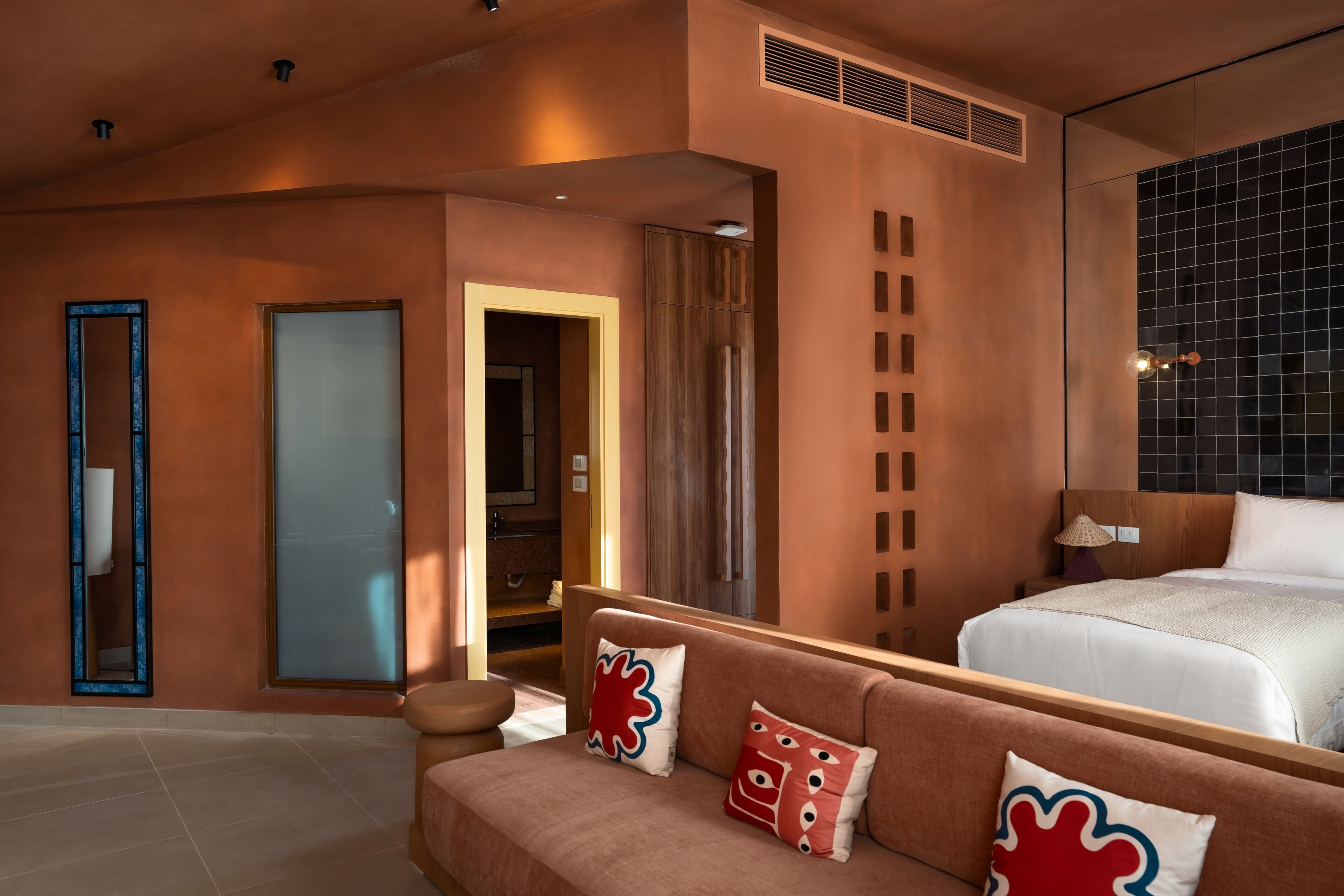 A hotel room with a bed, a sofa, a mirror, and a door.