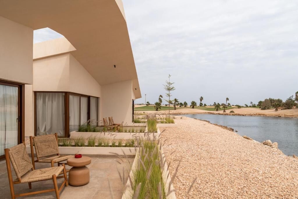 Un edificio moderno con patio, mobiliario exterior y vistas a un cuerpo de agua y al paisaje.