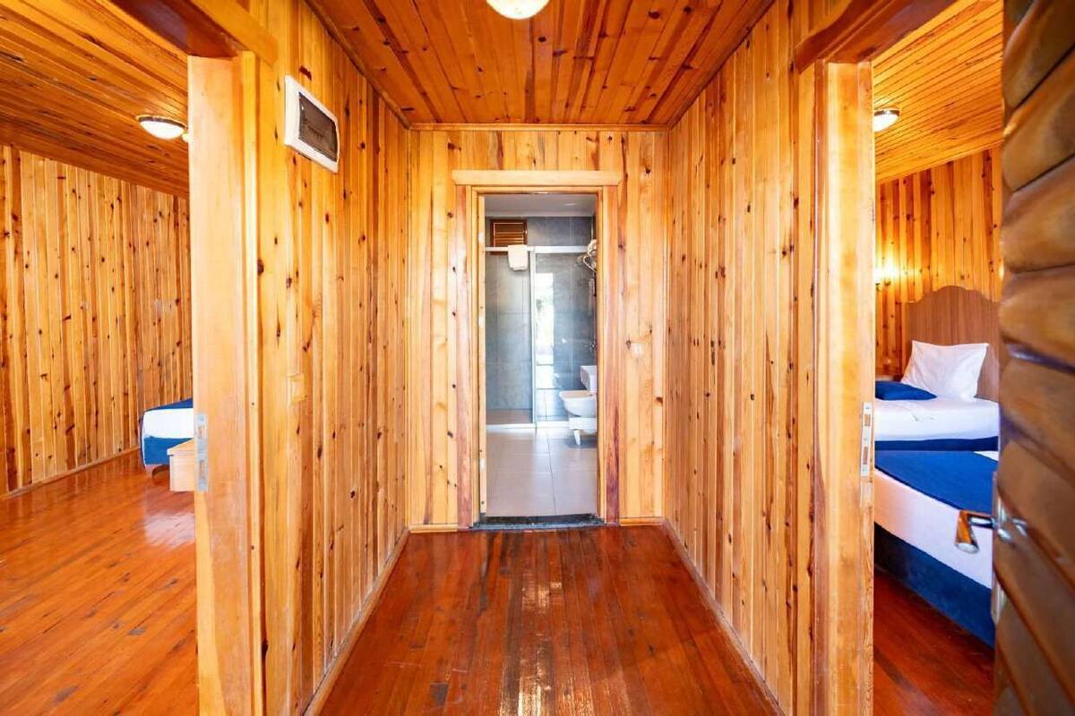 Interior de una cabaña de madera con un pasillo que lleva a un baño y una cama con cubierta azul.