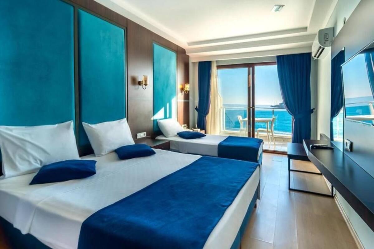 Habitación de hotel con dos camas, televisión, balcón con vista al mar y un amplio ventanal.