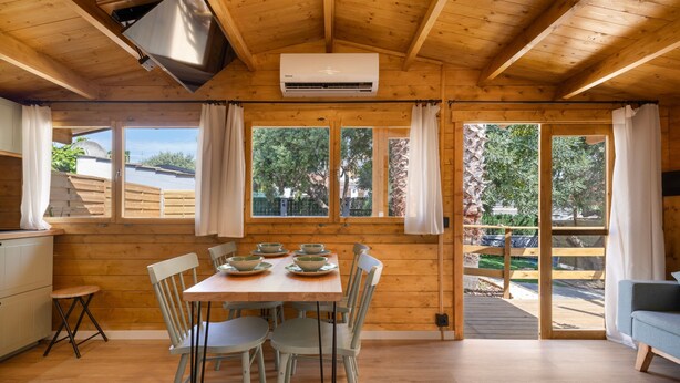 Un intérieur en bois avec une table à manger pour quatre personnes, un coin cuisine et de grandes fenêtres avec des rideaux.