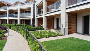 Un immeuble résidentiel à plusieurs étages, doté de balcons, d’une allée pavée et d’un jardin aménagé.