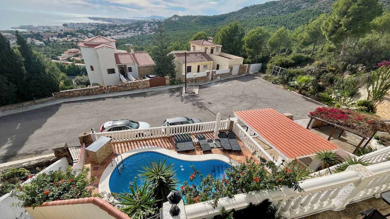 A rooftop pool with lounge chairs, a view of a town, and a hilly landscape.