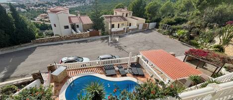 A rooftop pool with lounge chairs, a view of a town, and a hilly landscape.