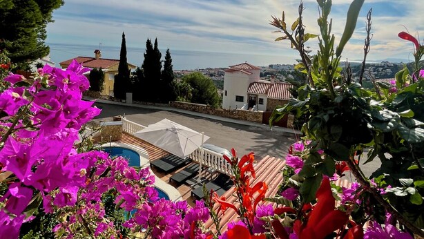 Eine Dachterrasse mit Pool, einem weißen Sonnenschirm und Blick auf das Meer und die Gebäude.
