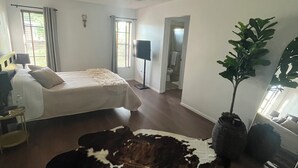 Ein Schlafzimmer mit einem Bett, einem Deckenventilator, einem Fenster mit Vorhängen, einer Pflanze und einem Kuhfellteppich.