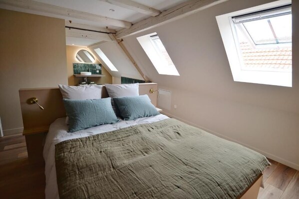 A bedroom with a bed, two skylights, a window, and a mirror.
