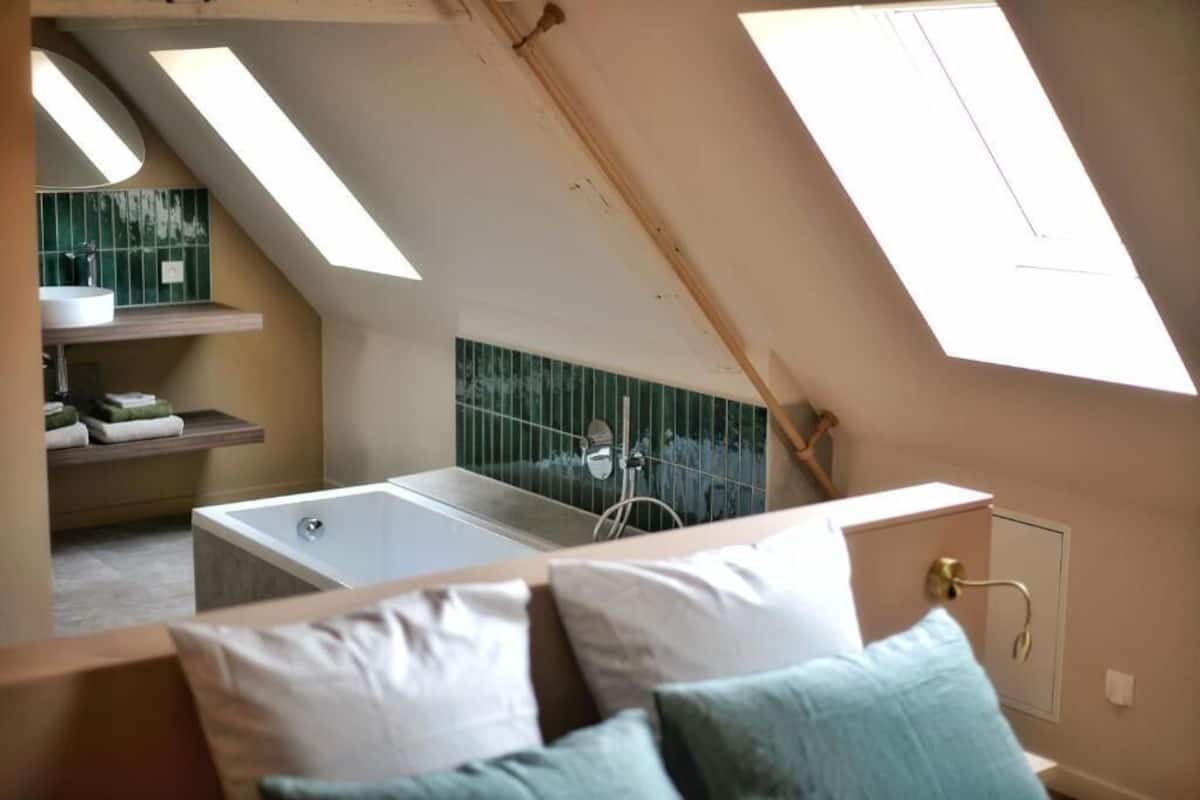 A bedroom with a skylight, a bathtub, and a view of a green-tiled shower area.