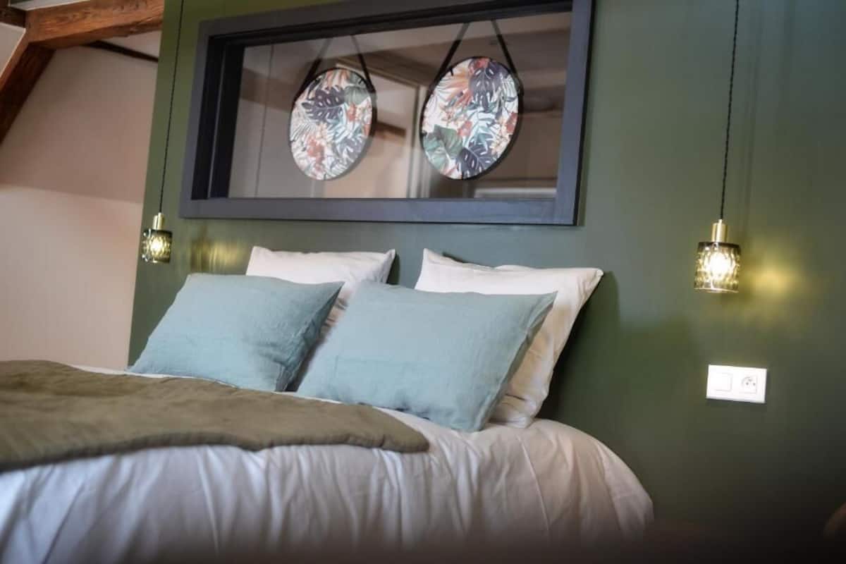 A bedroom with a bed, pillows, a framed artwork, and wall-mounted lights.