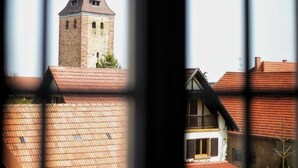 A view through a window of a building with a tower and a house with a red roof.