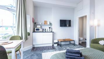 A compact hotel room with a kitchenette, a bed, a dining area, and a TV.
