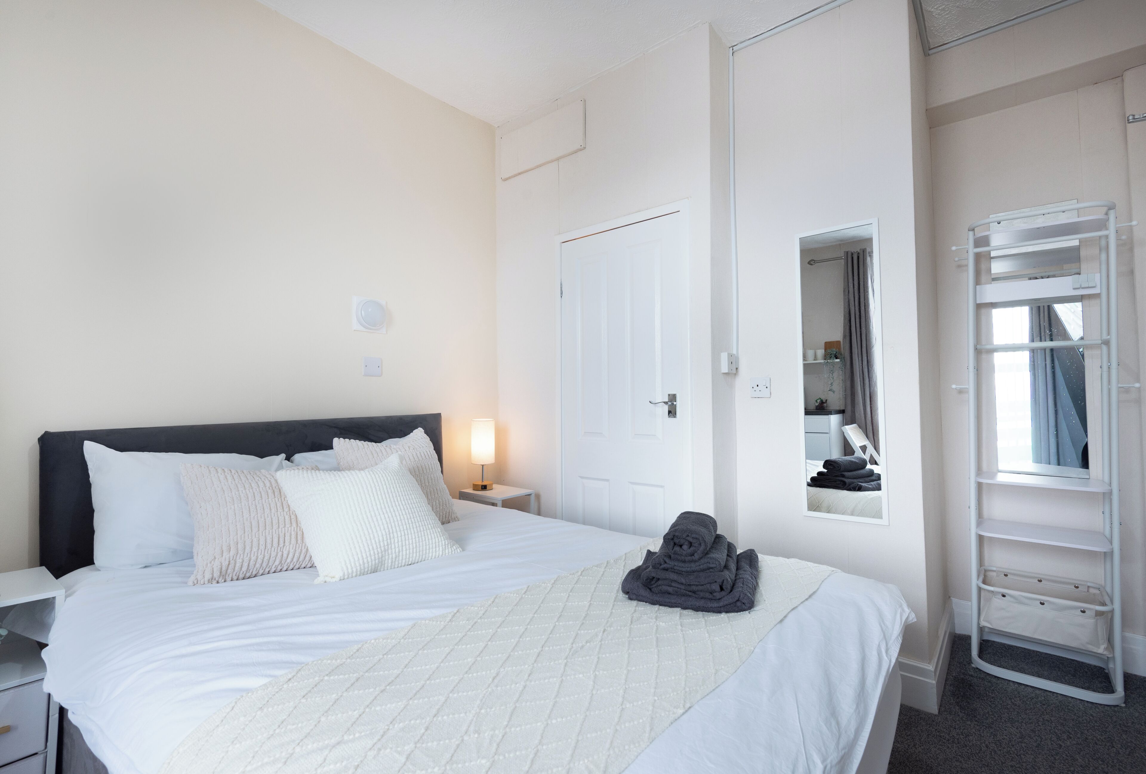 Een hotelkamer met een bed, nachtkastje, spiegel, raam en een inbouwplank.