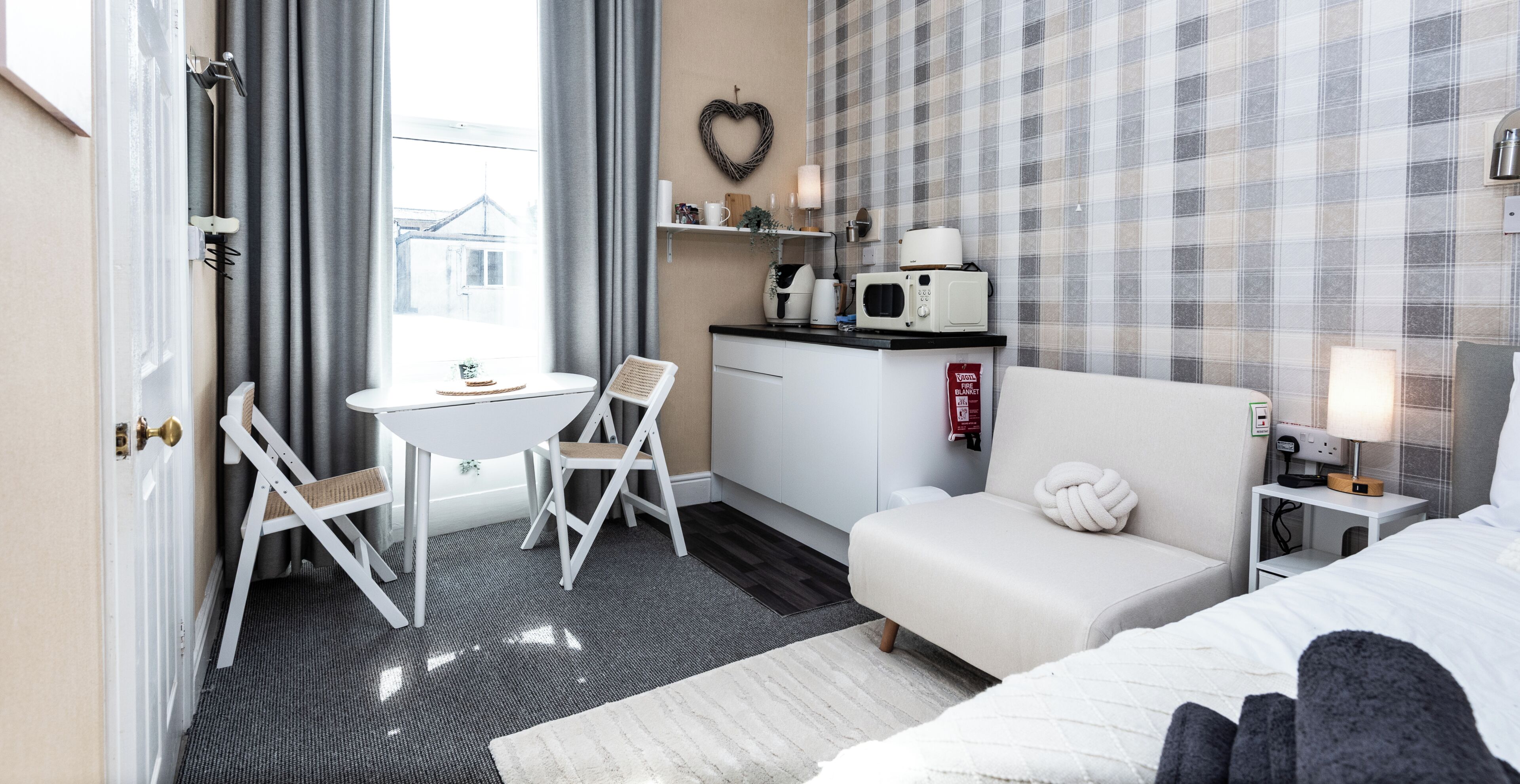 Ein Hotelzimmer mit Bett, kleinem Schreibtisch mit Stuhl, einer Küchenzeile und Blick durch ein Fenster.